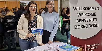 2 Frauen stehen vor einem Tisch und präsentieren Unterlagen