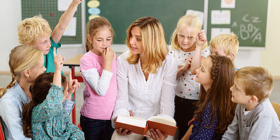 Eine Frau und Kinder sitzend auf dem Boden. Frau liest vor