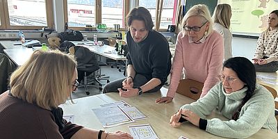 4 Personen stehen bzw. sitzen und schauen auf auf dem Tisch liegende Unterlagen